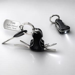May include: A set of car keys with a black multi-tool and a small flashlight. The multi-tool has several silver blades and a key. A silver tag reads "Tim Safe Drive! Love, Mom."