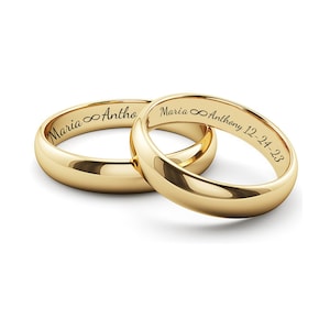 Puede incluir: Dos anillos de boda dorados con nombres y una fecha grabados. Un anillo dice "Maria &infin; Anthony 12-24-23". El otro anillo dice "Maria &infin; Anthony". Los anillos son lisos y brillantes, con un dise&ntilde;o cl&aacute;sico.