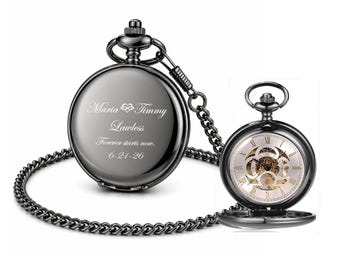 May include: Two dark gray pocket watches with chains. One watch is closed and engraved with the names "Maria & Timmy Lawless" and the date "6-21-26". The other watch is open, revealing the intricate clockwork and Roman numeral hour markers.