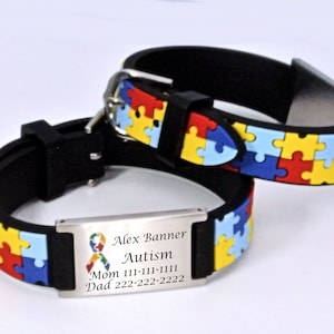 May include: Two black wristbands with a colorful puzzle piece pattern. One wristband has a metal plate with the words "Alex Banner Autism" and contact information. The puzzle pieces are red, yellow, blue, and green.