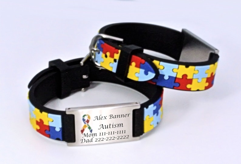 May include: Two black wristbands with a colorful puzzle piece pattern. One wristband has a metal plate with the words "Alex Banner Autism" and contact information. The puzzle pieces are red, yellow, blue, and green.