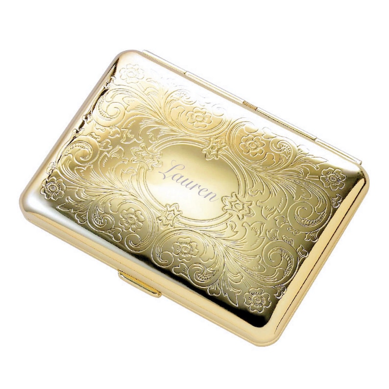 Puede incluir: Estuche de metal dorado para cigarrillos con un dise&ntilde;o floral grabado y el nombre "Lauren" en el centro.
