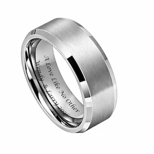 May include: A silver-colored ring with a brushed metal finish. The ring has a flat top and beveled edges. Engraved on the inside is the text "A Love Like No Other Wendy & Larry 2026".