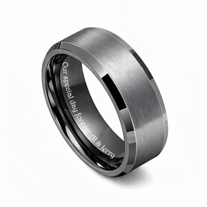 May include: A gray tungsten ring with a brushed finish and beveled edges. The inner band is black with the inscription "Our special day forever Al & Jerry". The ring has a modern, minimalist design.