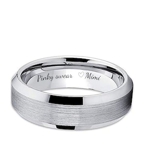 May include: A silver-colored ring with a brushed center band and polished edges. The inside of the ring is engraved with the words "Pinky swear" and "Mimi" with a heart symbol. The ring is a classic style.