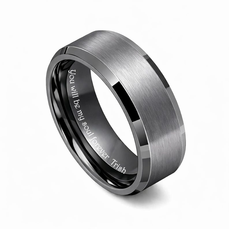May include: A gray tungsten ring with a brushed finish and a black interior. The ring has a beveled edge and the inscription "You will be my soul forever Trish" is engraved on the inside.