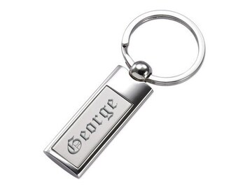May include: A silver rectangular keychain with the name "George" engraved in a gothic font. The keychain has a polished finish and a round key ring attached to a small ball.
