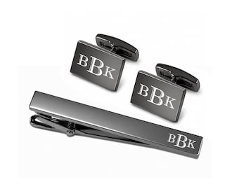 May include: A set of gunmetal-coloured accessories including two rectangular cufflinks and one tie bar. Each piece features a polished metallic finish and is engraved with the monogram letters BBK in a serif font, centred on the surface.