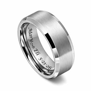 May include: A silver-colored ring with a brushed metal finish. The ring has a polished edge and engraved text inside that reads "Mary ∞ Eli 5-21-26". The ring is a wedding band or a similar type of jewelry.