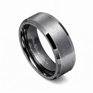 May include: A silver-colored ring with a brushed metal finish. The ring has a black interior with the engraved text "Ellie Kate &infin; Henry Forever Chicago". The ring has a beveled edge.