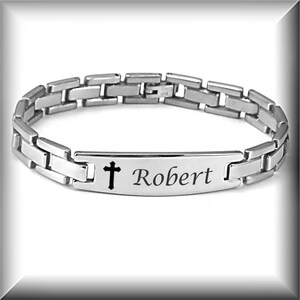 May include: Silver stainless steel bracelet with a cross and the name "Robert" engraved on a rectangular tag.