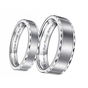 May include: Two silver wedding bands with a brushed metal finish. The rings have a geometric design on the edges and the inscription "My Love and Hope Forever 2026" inside. The infinity symbol is also included.