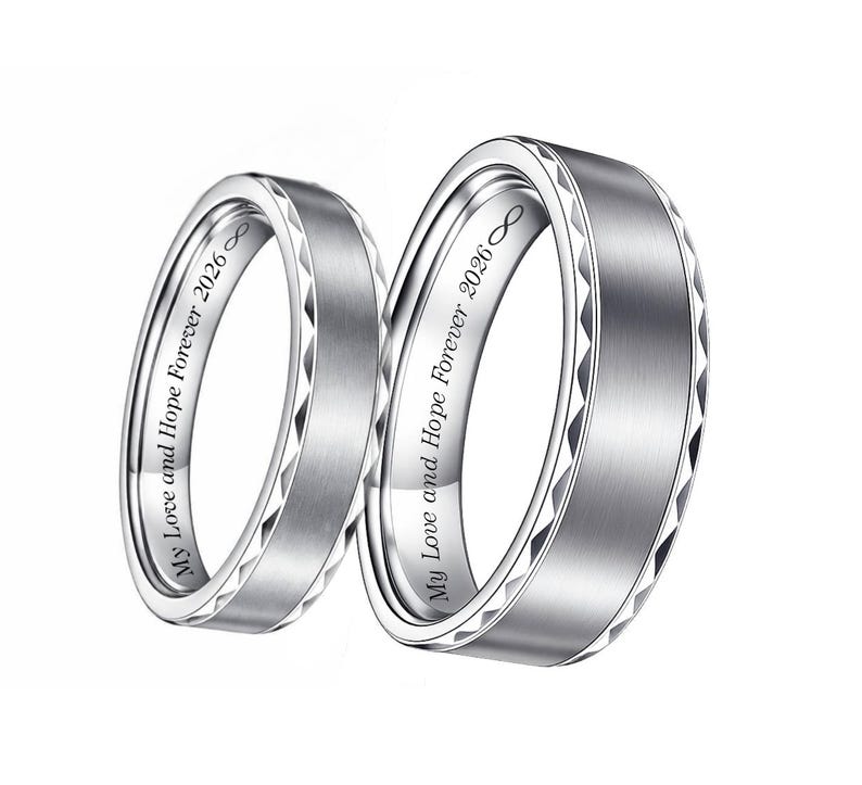 May include: Two silver wedding bands with a brushed metal finish. The rings have a geometric design on the edges and the inscription "My Love and Hope Forever 2026" inside. The infinity symbol is also included.