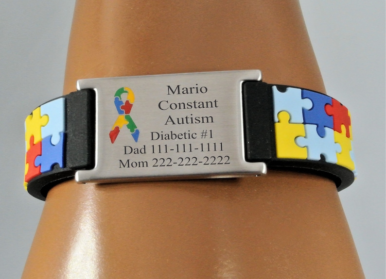 May include: A black and silver medical ID bracelet with a puzzle piece design. The bracelet has a silver plate with the words "Mario Constant, Autism, Diabetic #1" and contact information. The puzzle pieces are yellow, red, blue, and green.