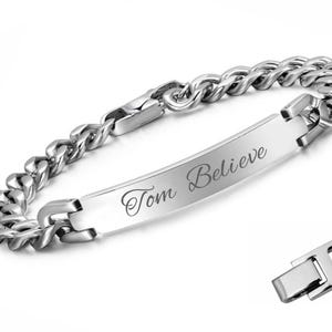May include: A silver-colored bracelet with a curb chain design. The bracelet features a rectangular plate engraved with the words "Tom Believe". A separate clasp is also visible. This piece of jewelry is suitable for everyday wear.