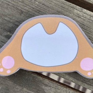 Puede incluir: Una pegatina de gato marrón y blanco con huellas de patas rosas. La pegatina tiene forma de cabeza de gato con una cara blanca y orejas marrones.