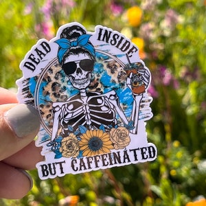 May include: A white sticker with a skeleton holding a coffee cup. The skeleton is wearing sunglasses and a blue bandana. The text on the sticker reads "Dead Inside But Caffeinated".