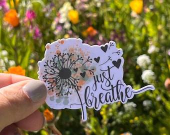 May include: A white sticker with a watercolor-style dandelion design and the text "just breathe". The dandelion has black stems and seeds, and there are small black hearts scattered around it.
