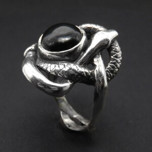May include: A silver ring with a black gemstone set in a snake design.