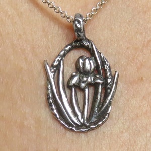May include: A silver necklace with a pendant featuring a stylized flower design. The pendant is shaped like a circle with a flower in the center and leaves around the edge.