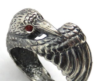 May include: A silver ring with a detailed design of a bird with outstretched wings. The bird's eye is a red gemstone.