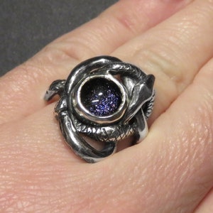 May include: A silver ring with a coiled snake design and a round, dark blue gemstone in the center.