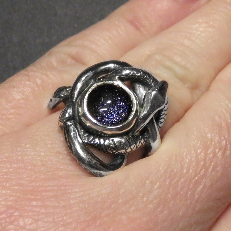 May include: A silver ring with a coiled snake design and a round, dark blue gemstone in the center.