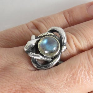 May include: A silver ring with a large, round, iridescent blue gemstone set in a snake design.
