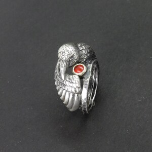 May include: A silver ring with a detailed bird design and a red gemstone in the center.