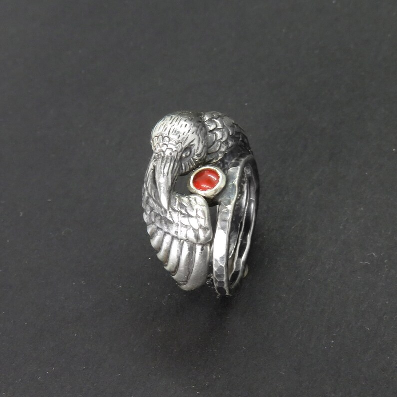 May include: A silver ring with a detailed bird design and a red gemstone in the center.