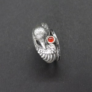 May include: A silver ring with a detailed bird design and a red gemstone. The ring is made of two bands, one with a textured finish and the other with a smooth finish.