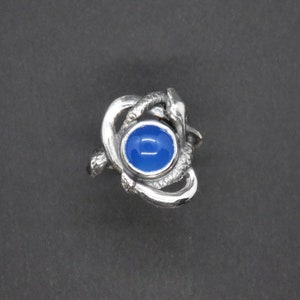 May include: A silver ring with a blue gemstone set in a design of intertwined snakes.