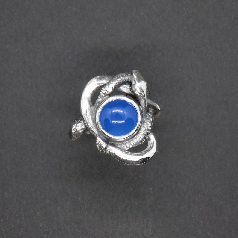 May include: A silver ring with a blue gemstone set in a design of intertwined snakes.