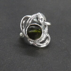 May include: A silver ring with a green gemstone set in a snake design.