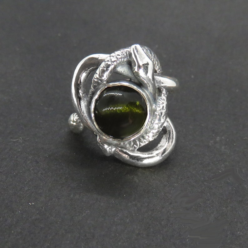 May include: A silver ring with a green gemstone set in a snake design.