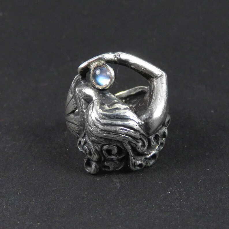 May include: A silver ring with a detailed design of a woman's head and a moonstone set in the ring.
