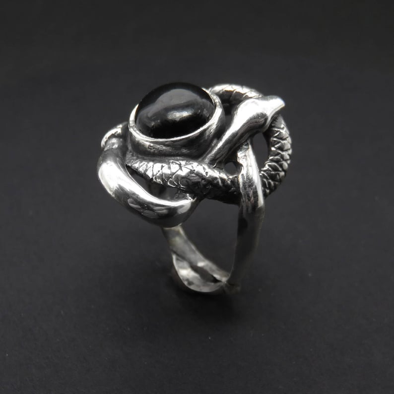 May include: A silver ring with a black gemstone set in a snake design.