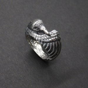 May include: A silver ring with a detailed design of a bird with its head tucked under its wing.