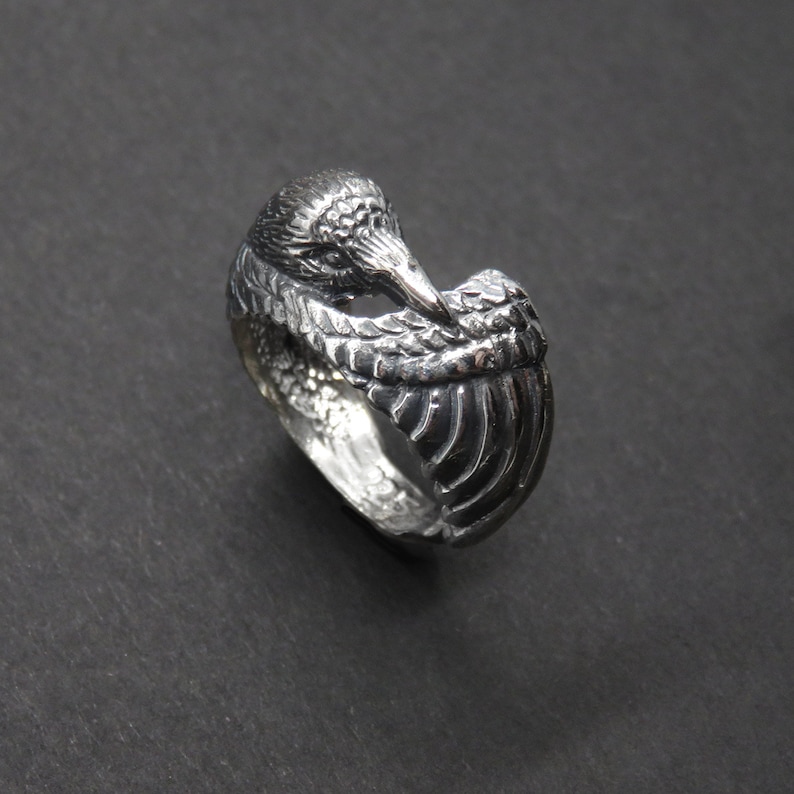 May include: A silver ring with a detailed design of a bird with its head tucked under its wing.