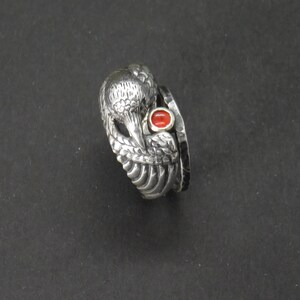 May include: A silver ring with a detailed bird design and a red gemstone. The ring is made of multiple bands.