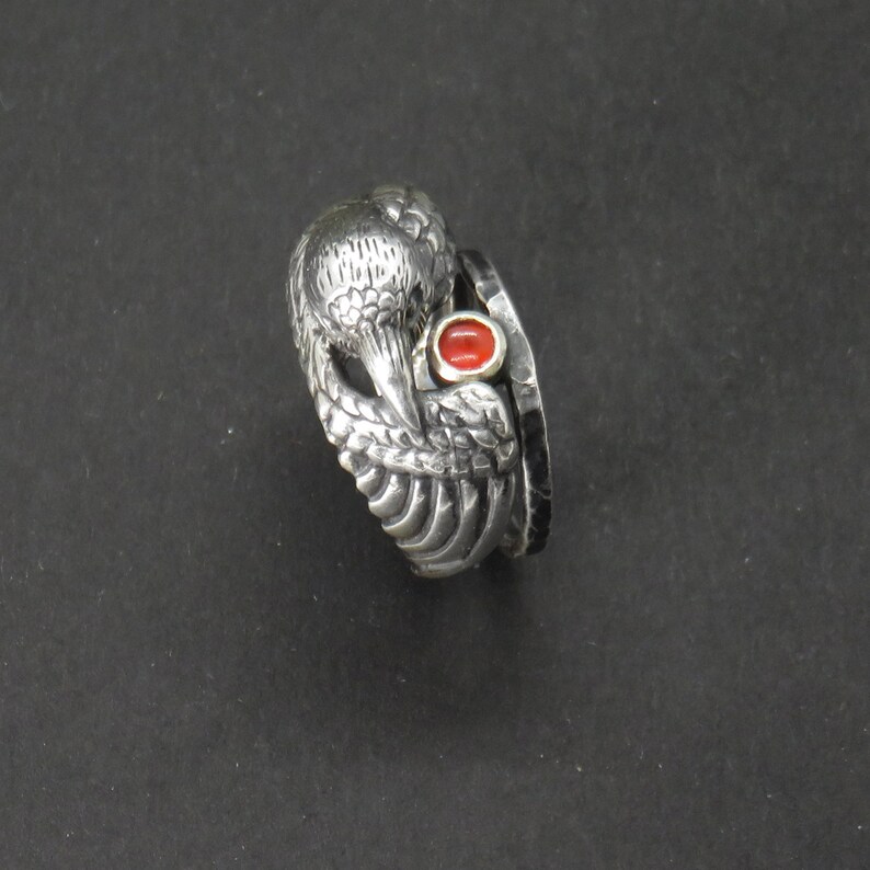 May include: A silver ring with a detailed bird design and a red gemstone. The ring is made of multiple bands.