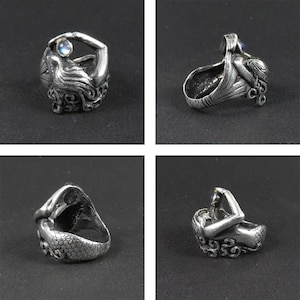 May include: A silver ring featuring a detailed mermaid design holding a pearl. The ring is shown from multiple angles.