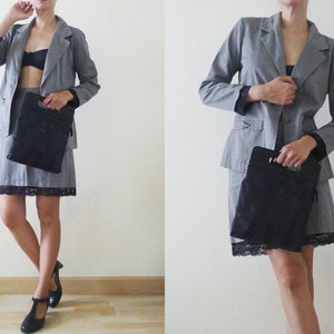 May include: A gray blazer and skirt suit with a black lace trim on the skirt. The suit is paired with a black handbag and black shoes. The outfit is a classic business attire.