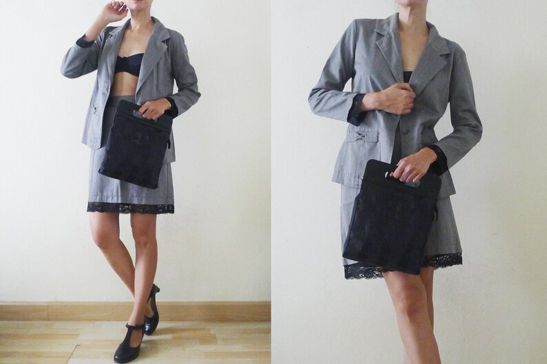 May include: A gray blazer and skirt suit with a black lace trim on the skirt. The suit is paired with a black handbag and black shoes. The outfit is a classic business attire.