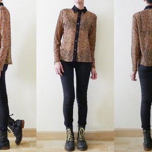 Op de afbeelding: Een doorschijnend overhemd met luipaardprint, een zwarte kraag en zwarte knopen. Het overhemd wordt gedragen met een zwarte skinny jeans en zwarte en gele veterschoenen.