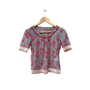 May include: A grey and red floral print blouse with short sleeves and a scoop neck. The blouse has a white lace trim around the neckline and sleeves.