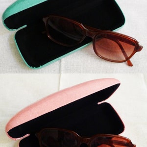 May include: Two pairs of sunglasses in their cases. The cases are open and the sunglasses are inside. The case on the top is teal and the case on the bottom is pink.