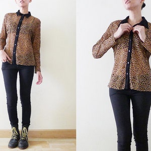 Op de afbeelding: Een doorschijnend overhemd met luipaardprint, een zwarte kraag en zwarte knopen. Het overhemd wordt gedragen met een zwarte jeans en zwarte veterschoenen.