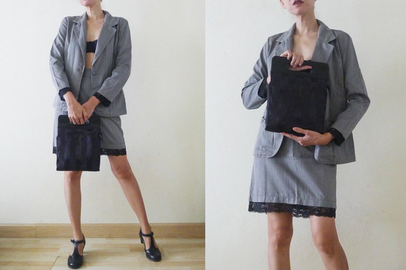 May include: A gray pinstripe blazer and skirt suit with black lace trim. The suit is paired with black heels and a black handbag. The outfit is worn by a person.