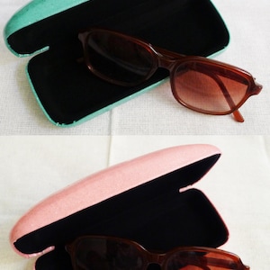 May include: Two pairs of sunglasses in their cases. The cases are open and the sunglasses are inside. The case on the top is teal and the case on the bottom is pink.